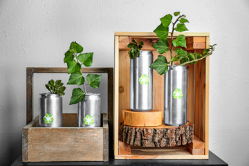 Tin cans with plants on table near light wall. Waste recycling concept