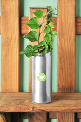 Tin can with plant on wooden shelf near color wall. Waste recycling concept