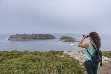 Naklejka na ściany i meble Girl with binoculars looking at Sisarga Islands (Malpica, La Coruna - Spain).