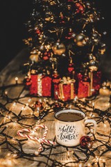 Close up of a white mug with christmas lights and christmas decorations on a wooden table with the message Hello winter