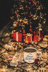 Close up of a white mug with christmas lights and christmas decorations with the message Merry Christmas