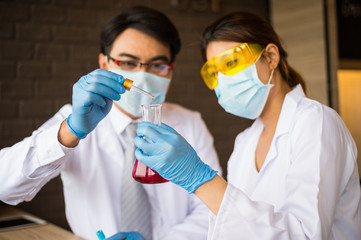 scientist man and woman wear white coat and blue gloves holding dropper and drop red water to tube science. Chemist examines chemical test tube, science, doctor