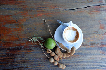 Cappuccino coffee in the white cup with coffee spoon and tamarind and green lemon on the wooden...
