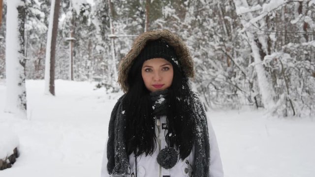 Portrait of a happy young brunette woman in the middle of a snowball fight getting a snowball in her face.