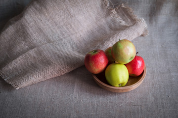 some apples in wooden plate on a linen tablecloth with burlap and ears of wheat 