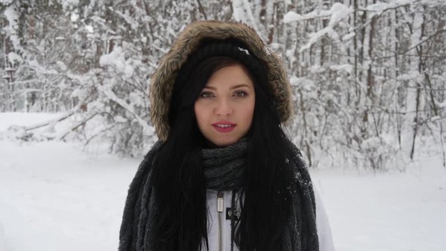 Portrait of a happy young brunette woman in the middle of a snowball fight getting a snowball in her face.