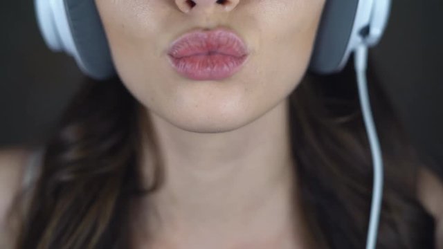 Face of sexy brunette close-up. A young woman in big white headphones is flirting with the camera. eroticly opens his mouth. chubby female lips. 4k