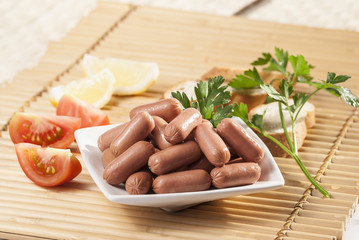 Chicken & Beef cocktail sausage with cherry tomato radish and lemon with green herb with toast bread on green red and bamboo background  with white and green plate