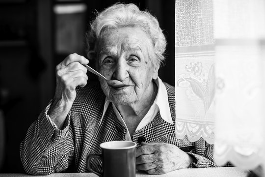 Elderly woman drinking tea sitting at the table. Black and white portrait.