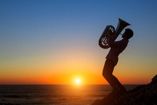 Silhouette of a musician play Tuba at sunset on sea shore.