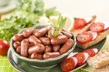 Chicken & Beef cocktail sausage with cherry tomato radish and lemon with green herb with toast bread on green red and bamboo background  with white and green plate