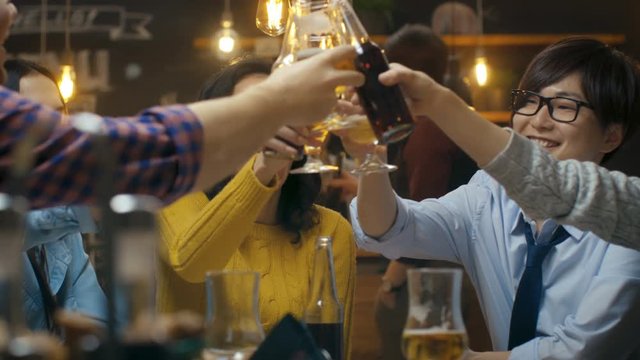 Diverse Group of Beautiful Young People Make a Toast and Clink Raised Glasses with Various Drinks in Celebration. In the Stylish Bar/ Restaurant. Shot on RED EPIC-W 8K Helium Cinema Camera.