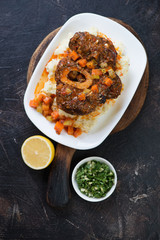 Plate with ossobuco and potato puree on a dark brown stone background, view from above, vertical shot