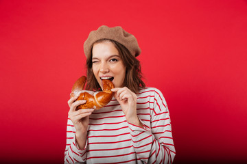 Portrait of a pretty woman wearing beret eating croissant