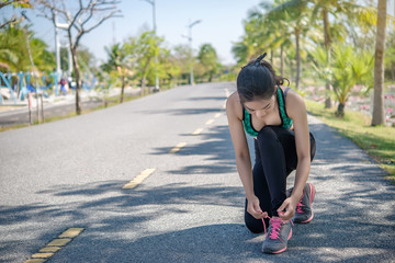 Beautiful asian sporty woman sitting to tie my shoelaces.Slim girl jogging in the park on daylight