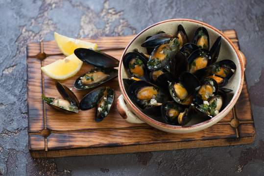 Bowl of freshly cooked mussels clams on a rustic wooden serving tray, studio shot, selective focus
