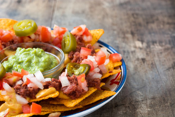 Mexican nachos with beef, guacamole, cheese sauce, peppers, tomato and onion in plate on wooden table