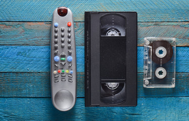 Video cassette, audio cassette, remote control on a blue wooden table. Retro media technology from...