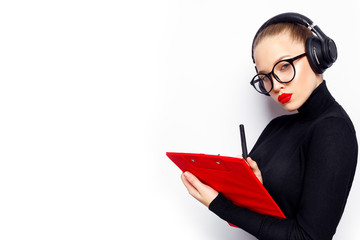Young office lady posing in black dress with headphones, pen in hand, red clipboard and red lips.
