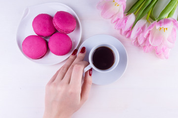 Female hand with a cup of coffee and flowers on a light table