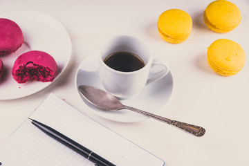 A cup of coffee and macaroon, flowers and notes on a light table