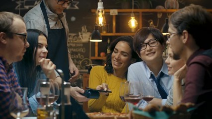 In the Bar Waiter Holds Credit Card Payment Machine and Beautiful Woman Pays for Her Order with Contactless Mobile Phone Payments System. She's Surrounded by Dear Friends and Has Time of Her Life.  - Powered by Adobe