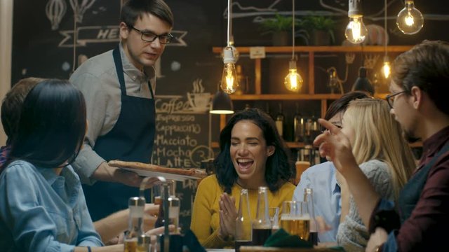 Waiter Serves Delicious Pizza to a Diverse Group Of Hungry and Happy Friends. They Eat, Drink and Have Fun in this Stylish Looking Bar. Shot on RED EPIC-W 8K Helium Cinema Camera.