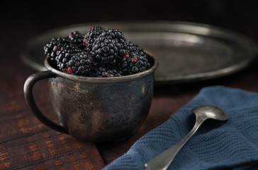 Fototapeta na wymiar blackberry bowl dark wood cup rustic moody pewter spoon