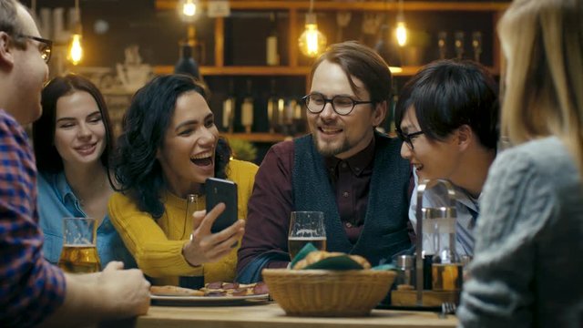 Beautiful Hispanic Woman Shows Interesting Stuff on Her Smartphone to Her Friends while They Have Good Time in Bar. Shot on RED EPIC-W 8K Helium Cinema Camera.