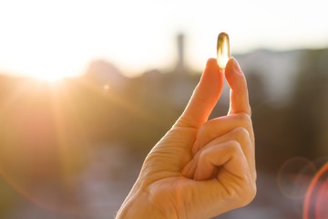 Fototapeta Hand of a woman holding fish oil Omega-3 capsules, urban sunset background. Healthy eating, medicine, health care, food supplements and people concept obraz