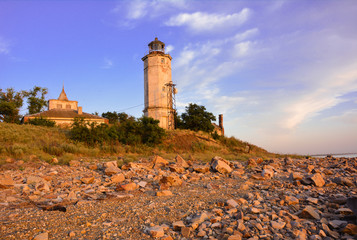 Old lighthouse on a stony seashore in summer at sunset