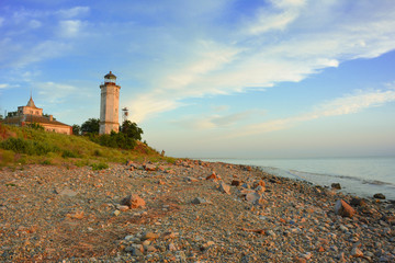 Old lighthouse on a stony seashore in summer at sunset