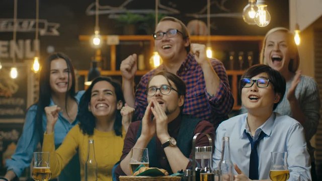 Diverse Group of Friends Watches TV in the Sporstbar. Beautiful Young People Drink, Have Fun and Cheer for their Team. Shot on RED EPIC-W 8K Helium Cinema Camera.