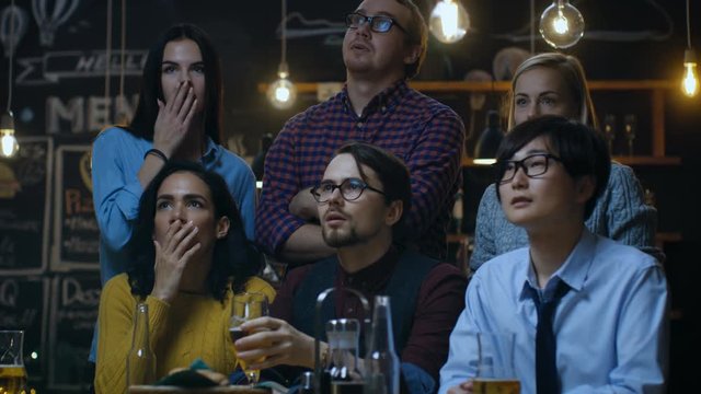 Young People in the Bar Watch TV Suddenly Breaking News Show that Tragic Events Unfold. Young People Are Horrified, Saddened and Shocked. Shot on RED EPIC-W 8K Helium Cinema Camera.