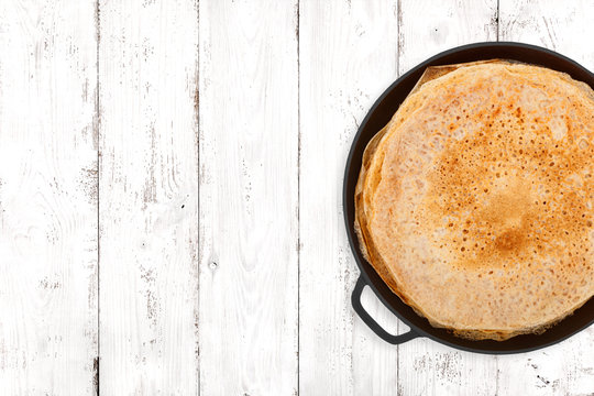 Crepes in a cast iron pan on light wooden background, top view