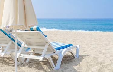 Sun umbrella and chaise longue on sea beach. White sand and sea in tropical resort. The concept of beach holiday. Relax and vacation.
