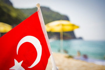 Turkish flag on background of sea beach on sunny summer day. Concept of tropical resort and rest on the beaches of Turkey. Summer holidays in Turkey.