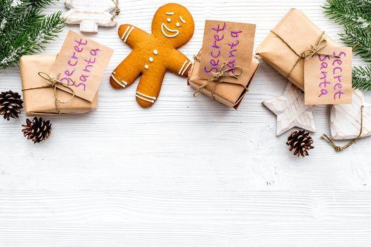 Christmas game Secret Santa. Gift boxes near spruce branch and gingerbread cookies on white wooden background top view copyspace