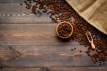 Fresh roasted coffee beans in bowl and scoop near canvas on dark wooden background top view copyspace