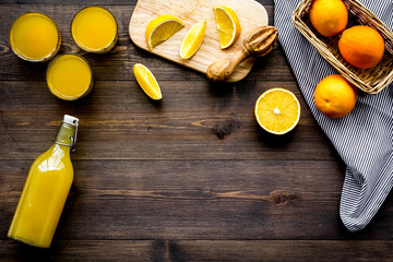 Healthy vitamin drink. Fresh orange juice near fruits and juicer on dark wooden background top view copyspace