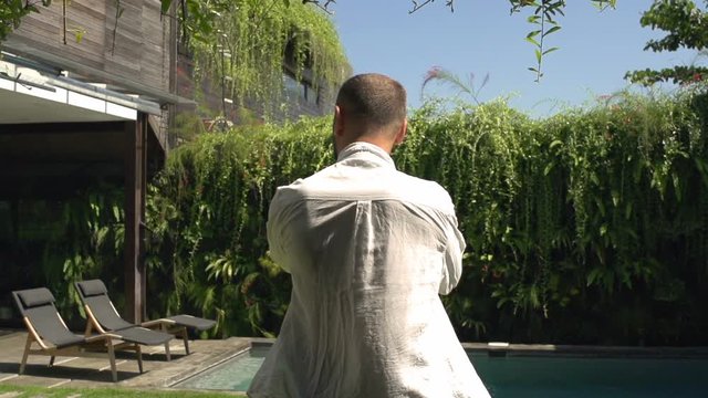 Man standing in the garden and puts shirt on, steadycam shot, slow motion shot at 240fps
