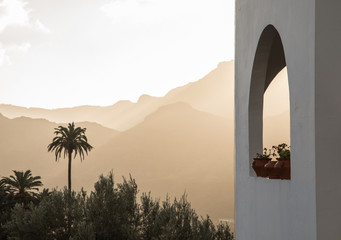 White building with arch window with plants, palm trees and mountains in the background