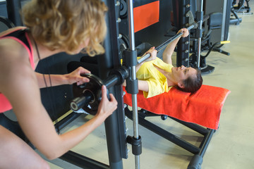 fitness-trainer assisting young female in lifting barbell in the gym