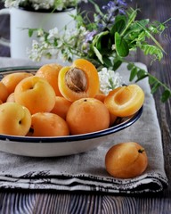 Naklejka na ściany i meble On a wooden table on a platter of fresh apricots with bones, decorated with flowers