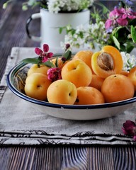 On a wooden table on a platter of fresh apricots with bones, decorated with flowers