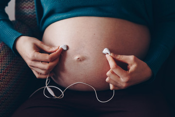 young mother to be holding earphones to her belly. baby belly listening to music through headphones. concept for prenatal care