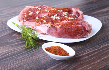 Raw pork steaks on wooden board with herbs, garlic and spices ready for cooking. Selective focus.