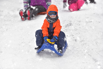 Fototapeta na wymiar Little boy riding on snow slides in winter time