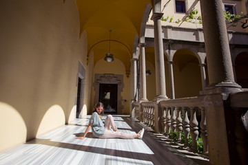 Traveller girl sitting on the floor in European  architecture building, enjoying summer day and and resting