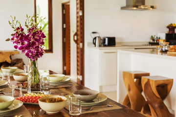 Luxury interior design in living room  villa. Bright space with high raised ceiling and wooden dining table. Simple asian style lunch, orchids in glass bottle